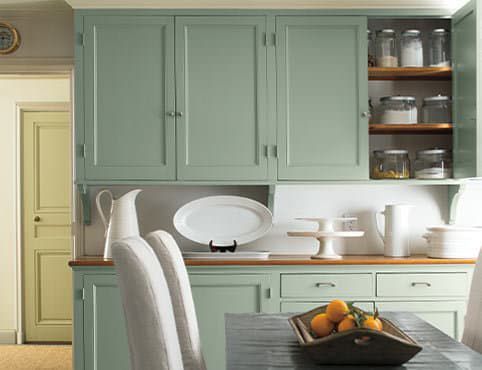 A kitchen with green cabinets and a bowl of oranges on the table.