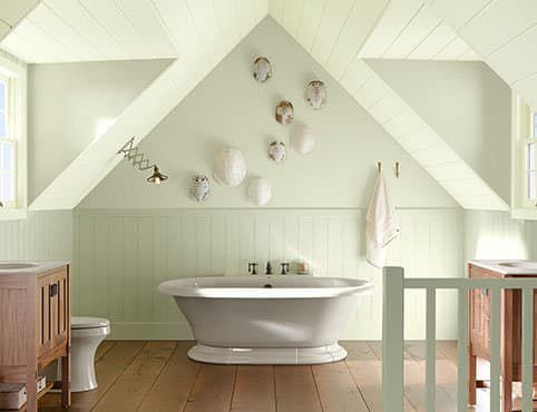 A bathroom with a bathtub, toilet, sink and attic ceiling.