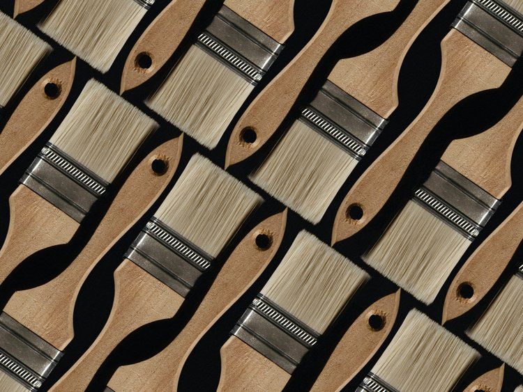 A bunch of paint brushes are lined up on a wooden table.