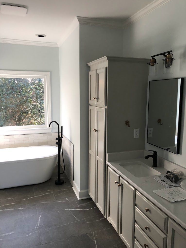 A bathroom with a tub , sink , mirror and cabinets.