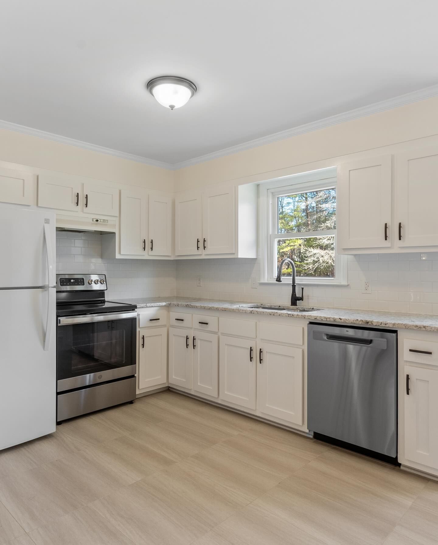 A kitchen with white cabinets , stainless steel appliances , a refrigerator , stove , sink and dishwasher.