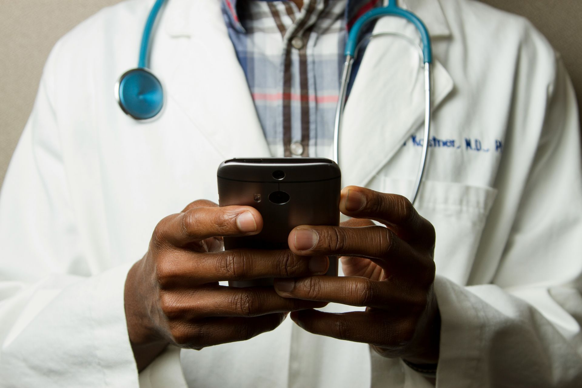 A doctor with a stethoscope around his neck is holding a cell phone in his hands.