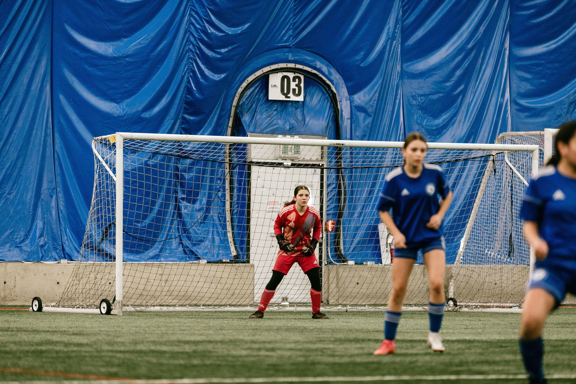 A group of young girls are playing soccer in an indoor stadium.