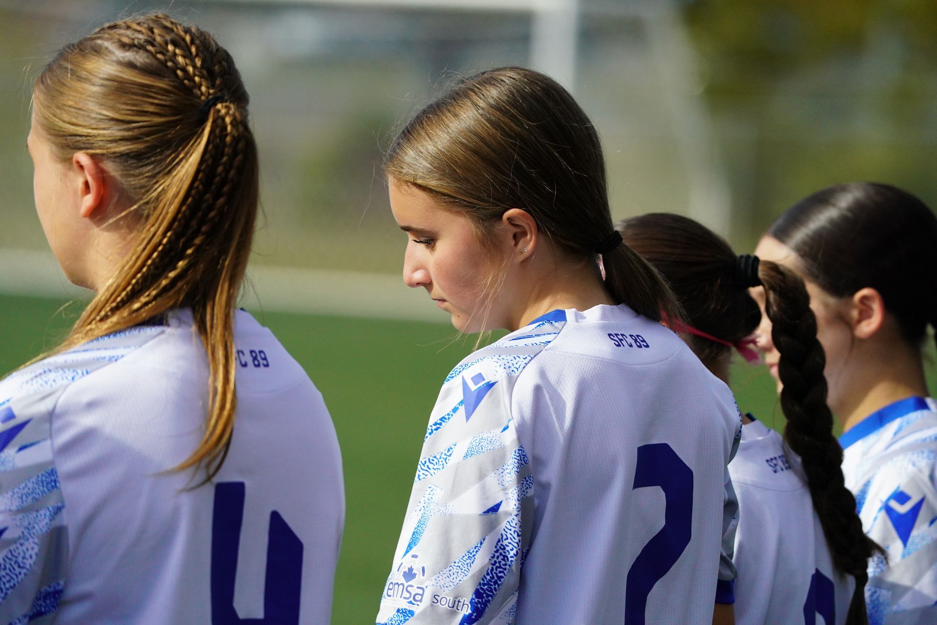Four soccer players in matching white and blue jerseys stand on a green field during a game.