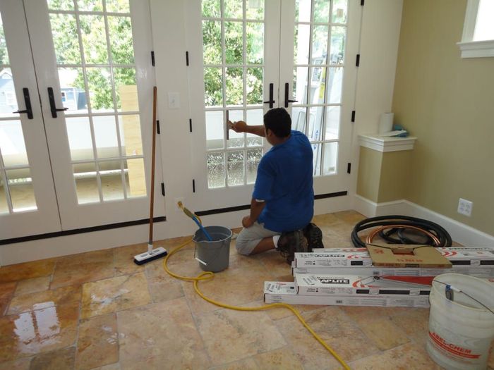 A man is kneeling down in a room cleaning a window