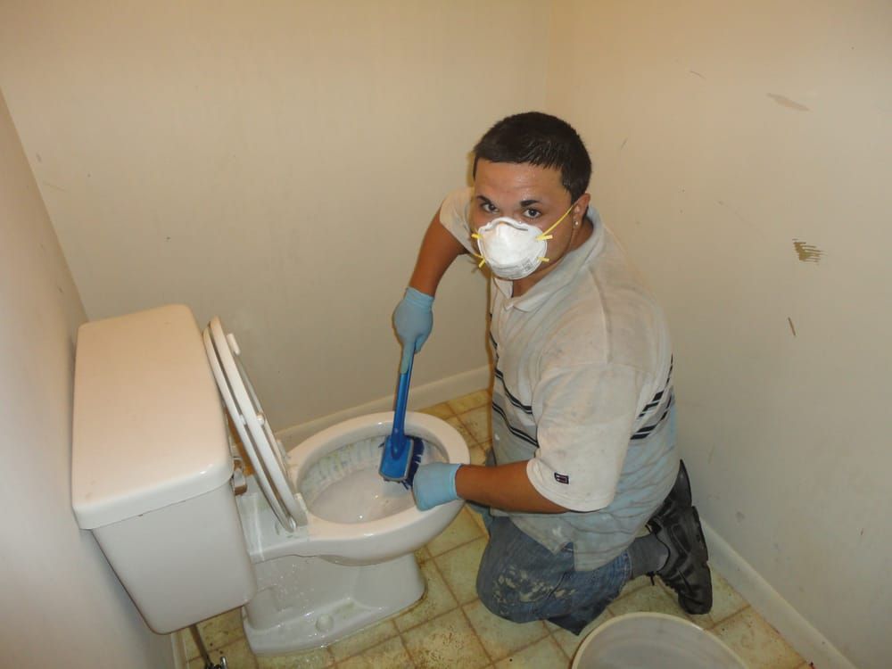 A man wearing a mask is cleaning a toilet with a brush.