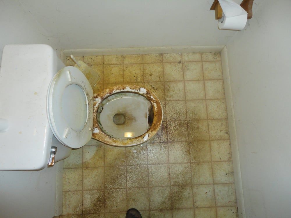 A toilet is sitting on a dirty tiled floor in a bathroom.