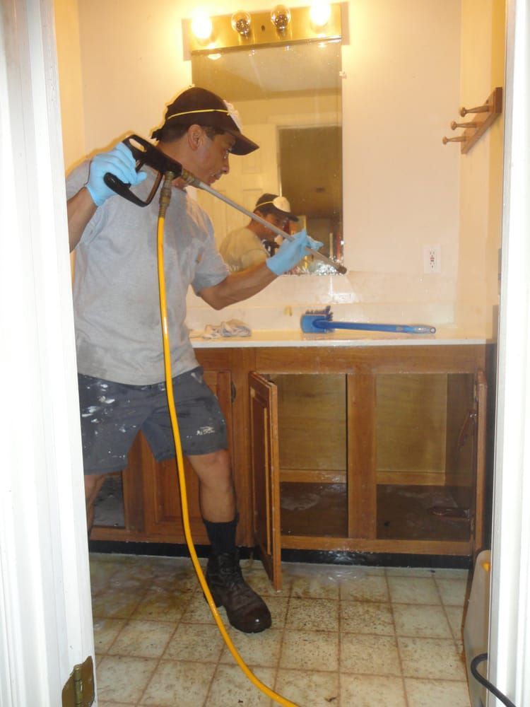 A man is spraying something in a bathroom with a hose