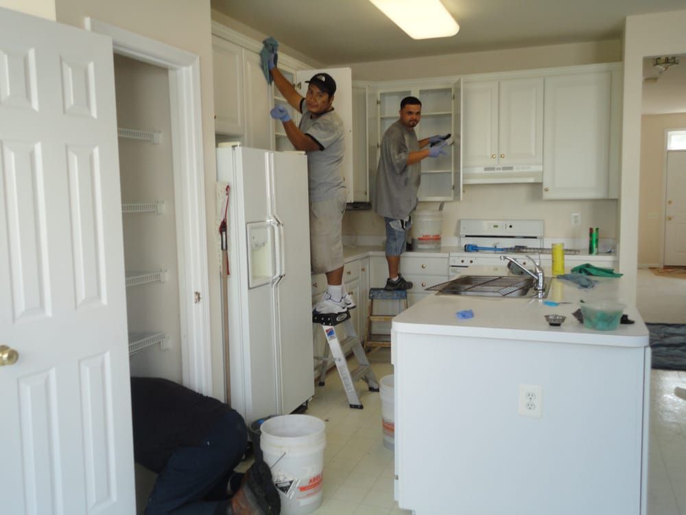 Two men are cleaning a refrigerator in a kitchen.