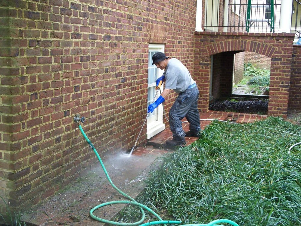 A man is cleaning a brick wall with a hose