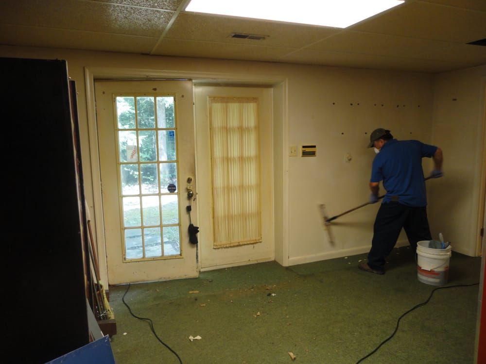 A man in a blue shirt is cleaning a room with a rake