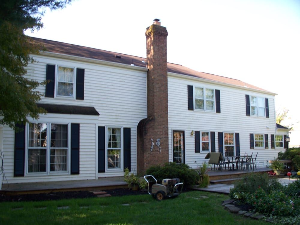 A white house with black shutters and a brick chimney