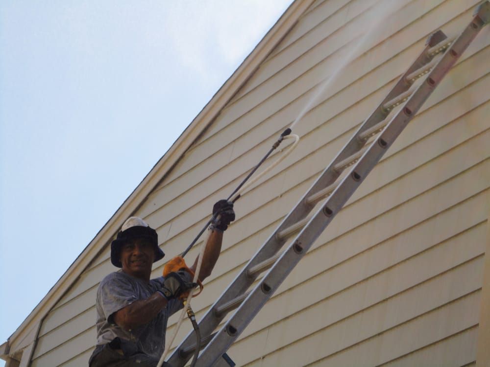 A man on a ladder spraying a house with a high pressure washer