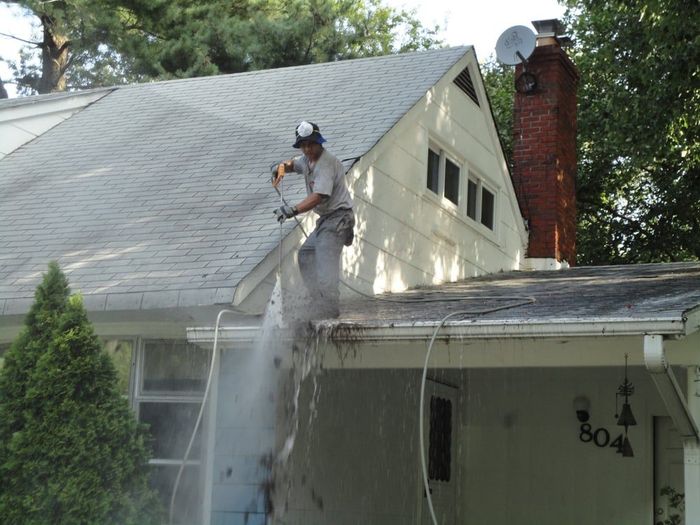 A man is cleaning the roof of a house with a hose