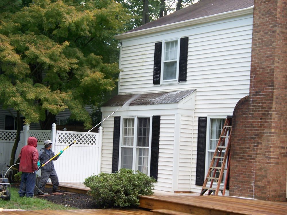 A white house with black shutters is being cleaned by two men