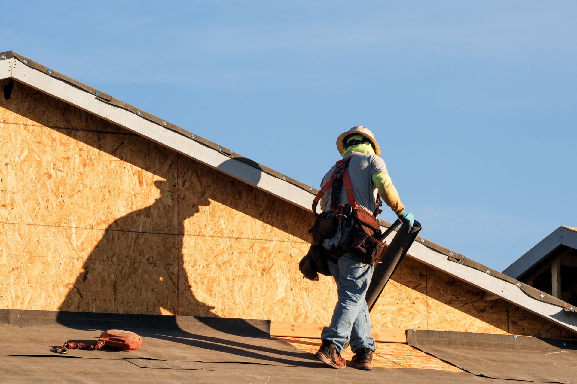 Construction worker installs roofing underlayment on a wood framed house under construction.