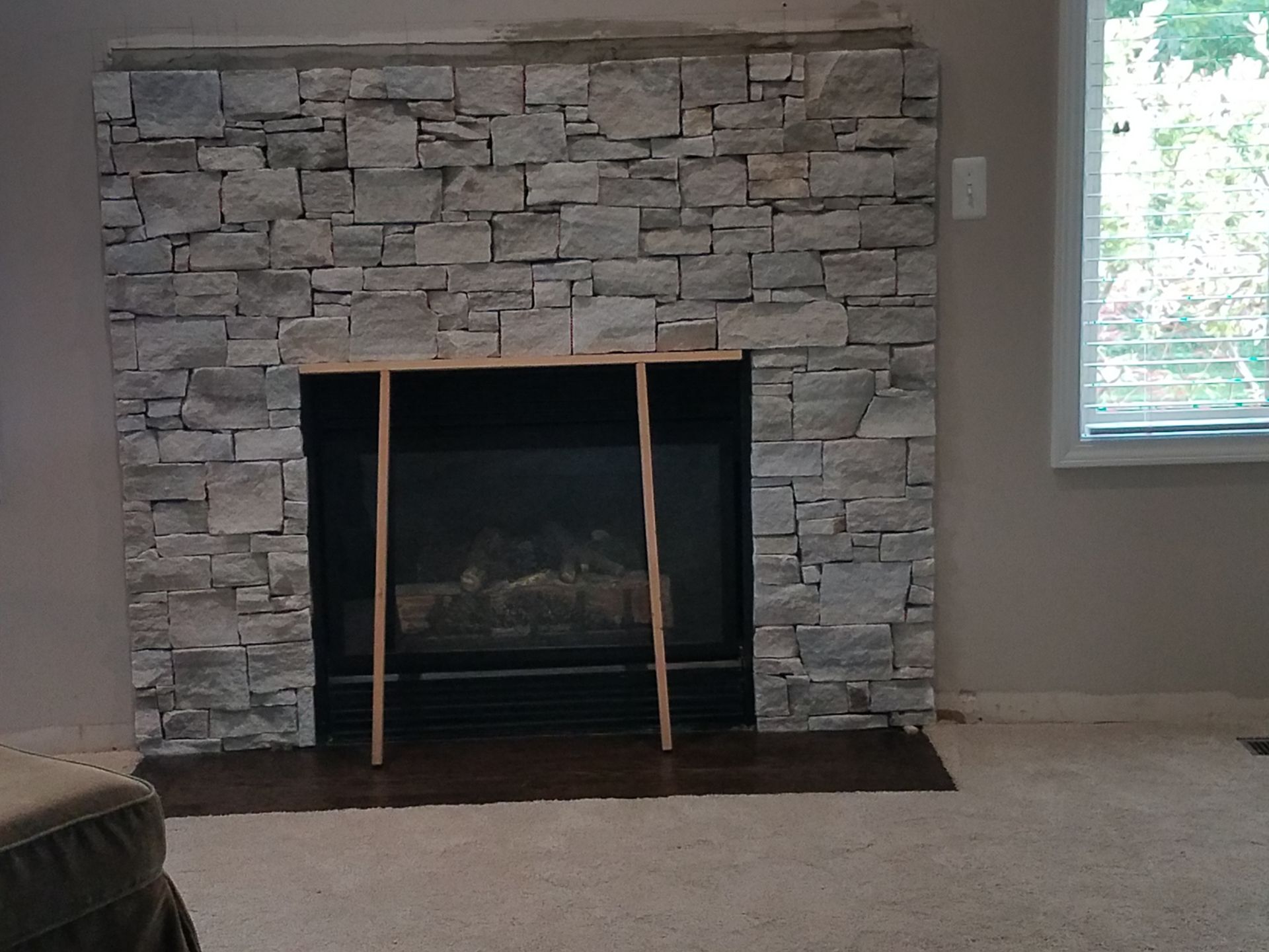 A living room with a stone fireplace and a window.
