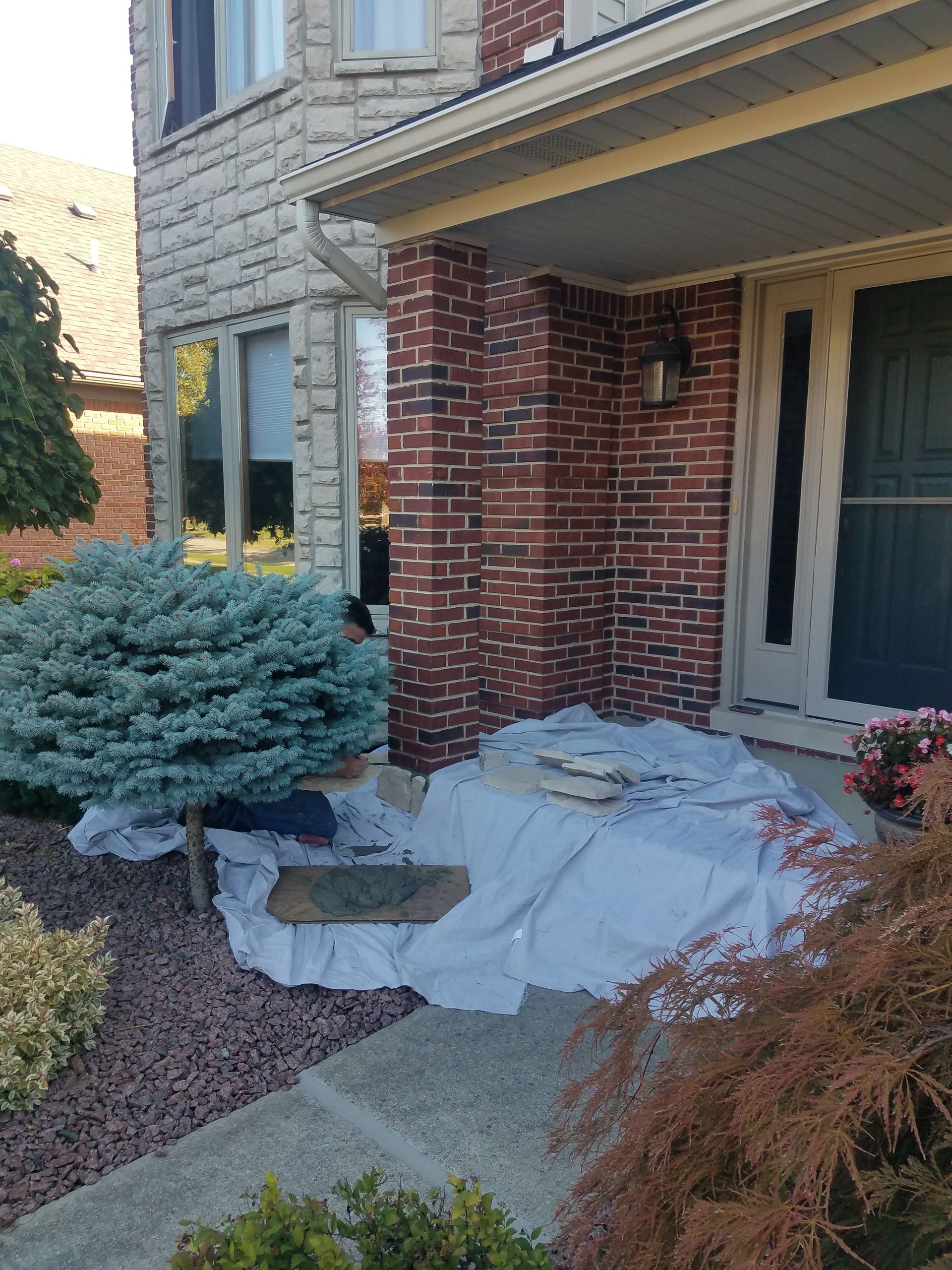 A brick house with a white tarp on the sidewalk in front of it.