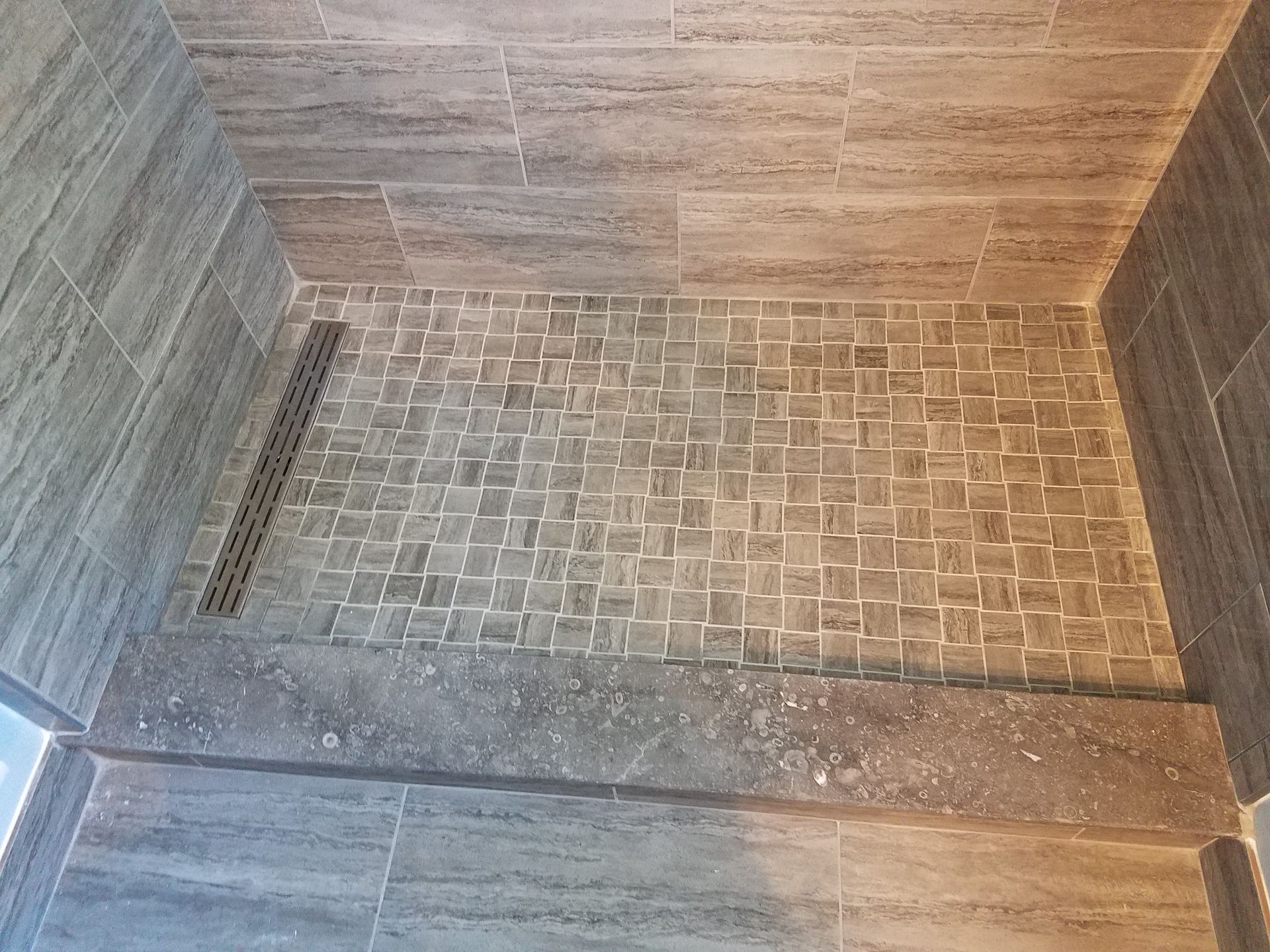 A walk in shower with a tiled floor and a drain.