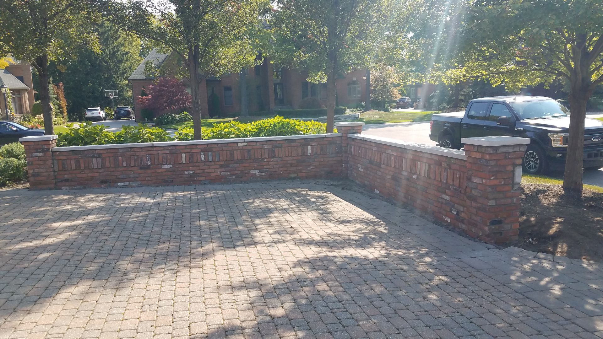 A black truck is parked in a driveway next to a brick wall.