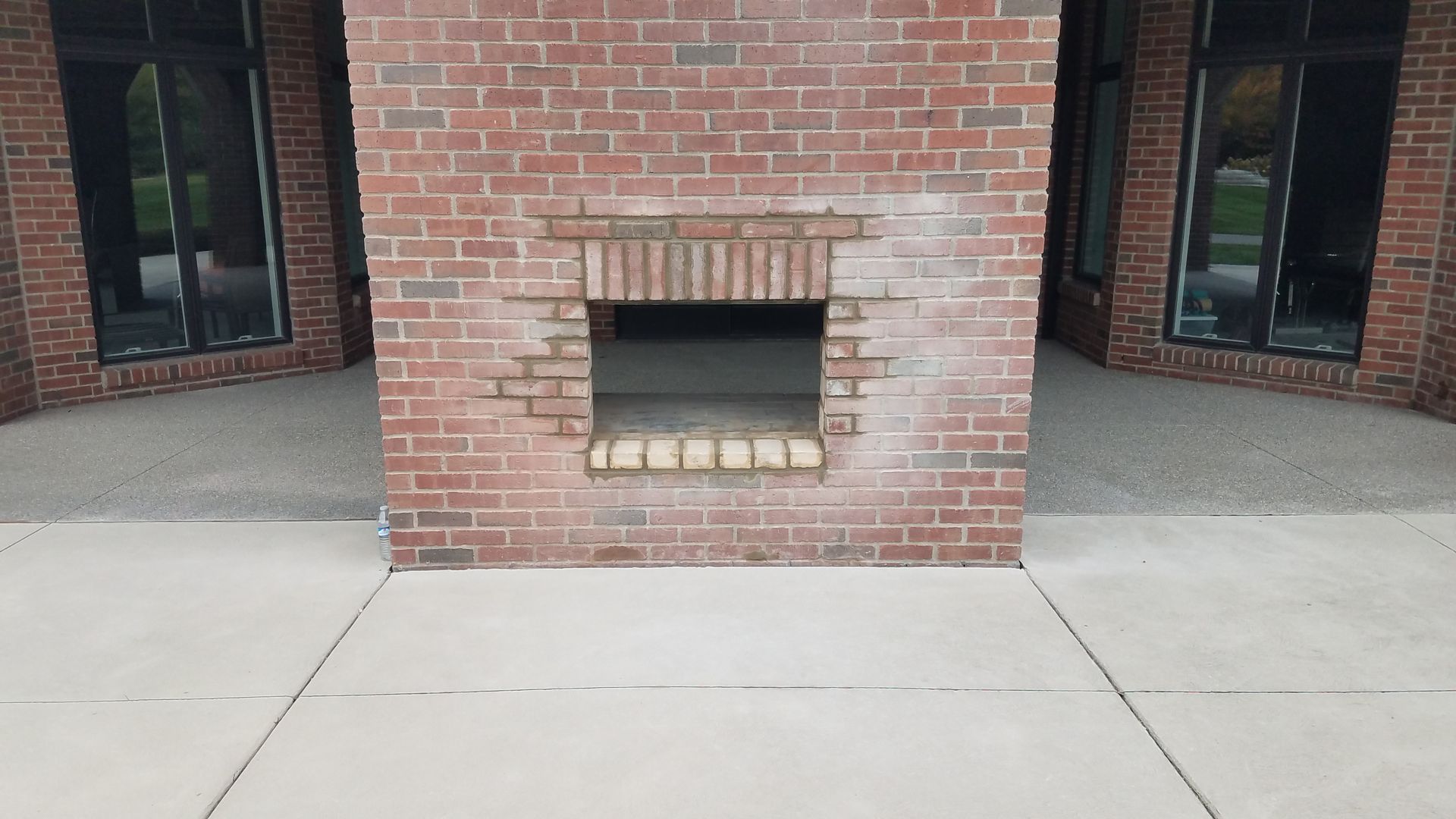 A brick fireplace with a hole in it is sitting on a concrete patio.