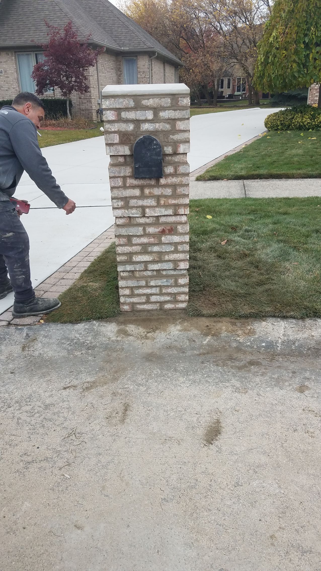 A man is measuring a brick post in front of a house.