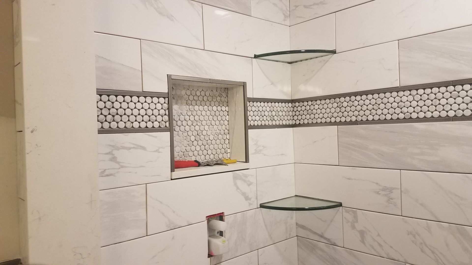 A bathroom with white tiles and glass shelves.
