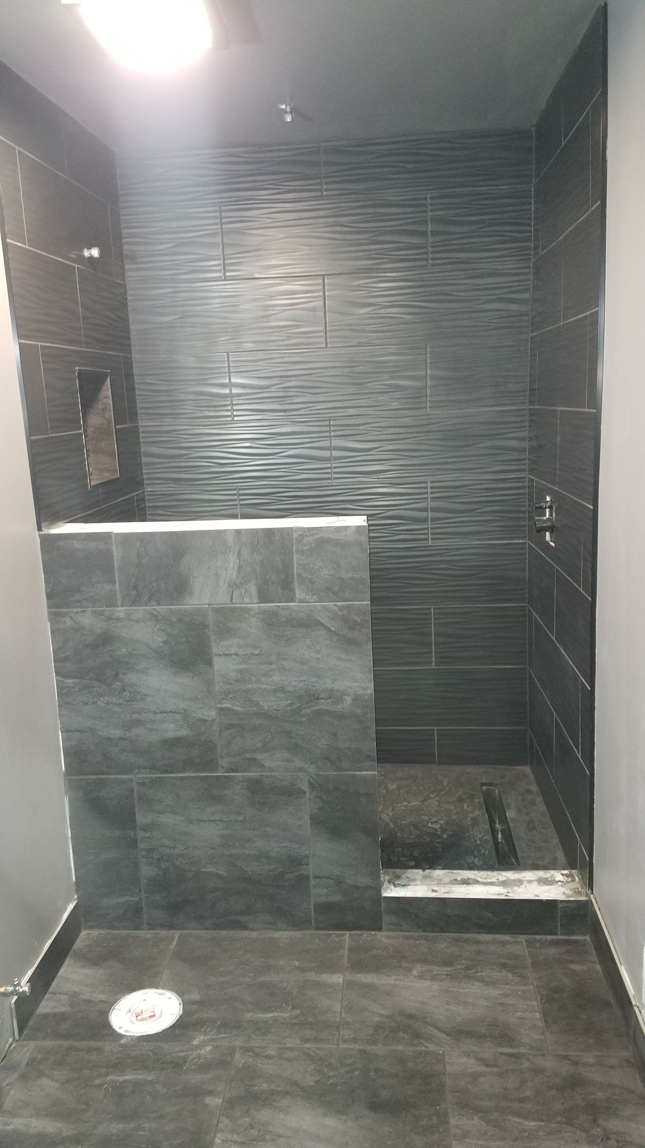 A bathroom with black tiles and a walk in shower.