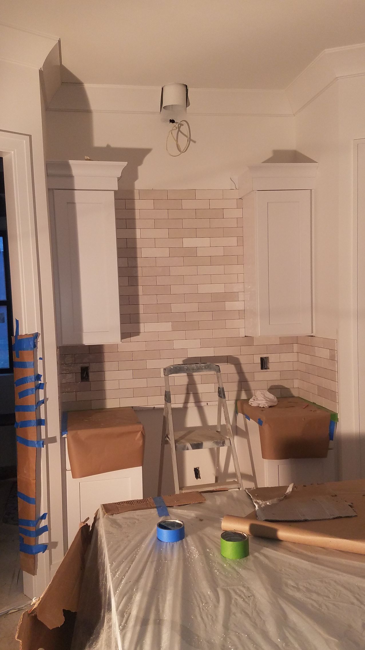 A kitchen under construction with a ladder , boxes , and tape.