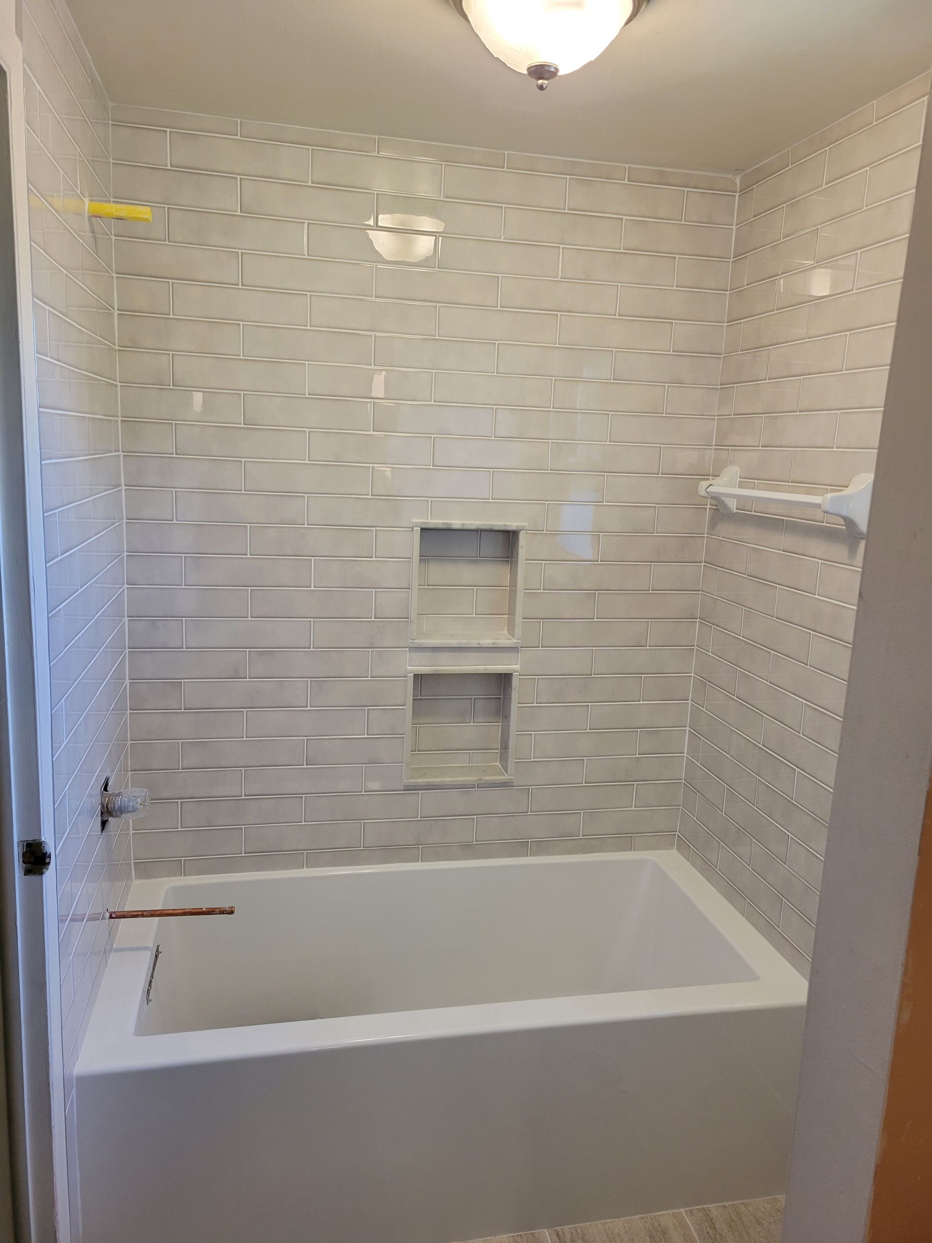 There is a bathtub in the shower with a brick wall behind it.