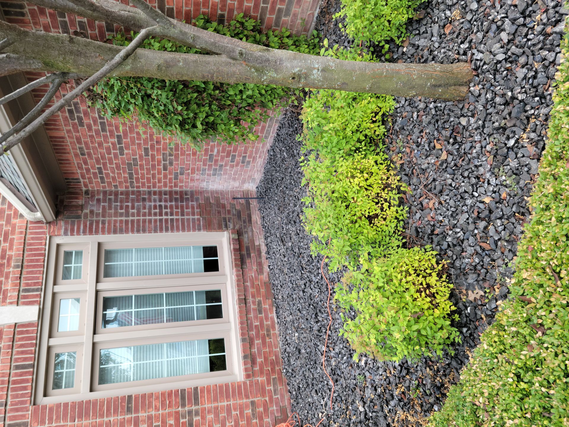 A brick building with a window and bushes in front of it.