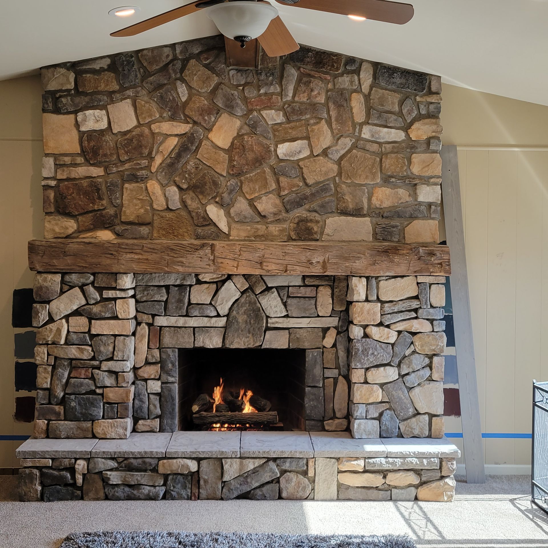 A stone fireplace with a ceiling fan above it