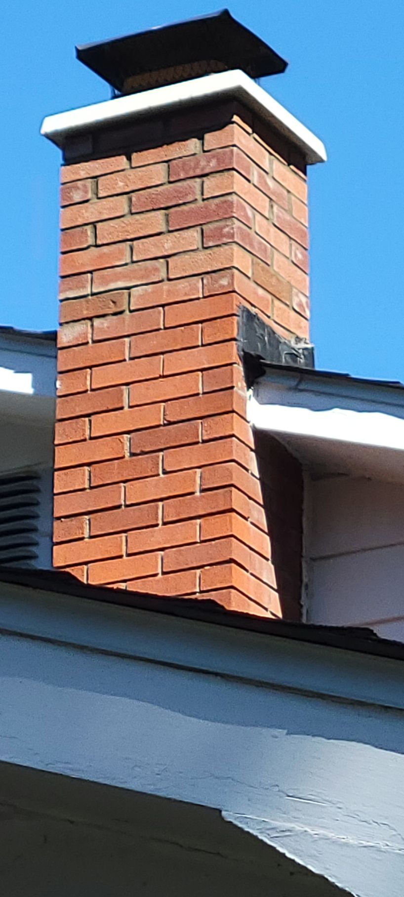 A brick chimney on top of a house with a blue sky in the background