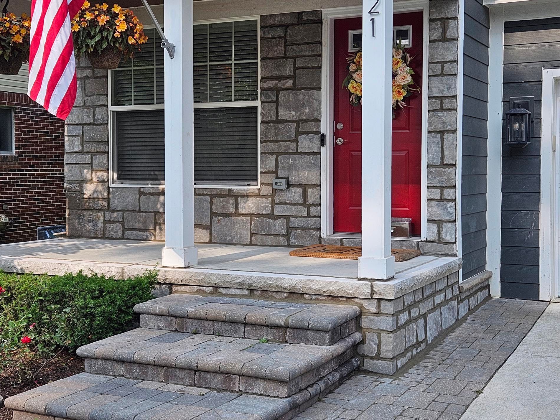 The front porch of a brick house with a red door