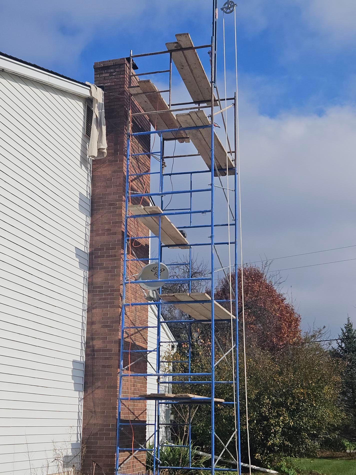 A blue scaffolding is being used to repair a chimney on the side of a house.