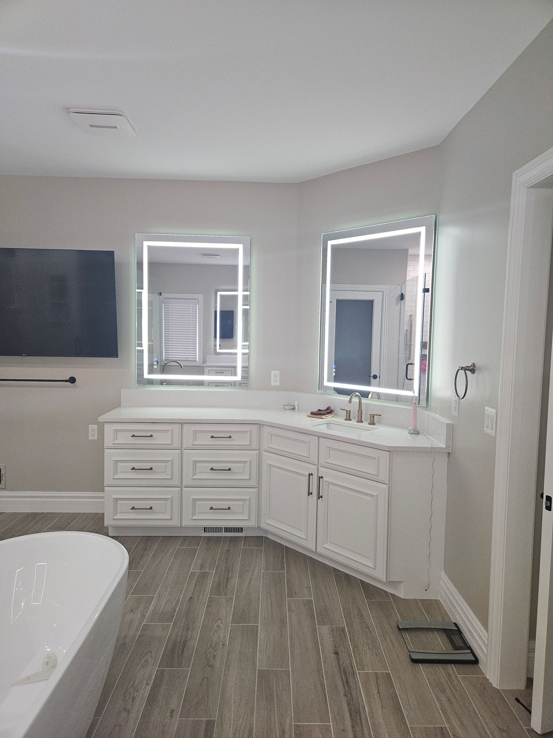 A bathroom with a tub , sink , mirror and television.