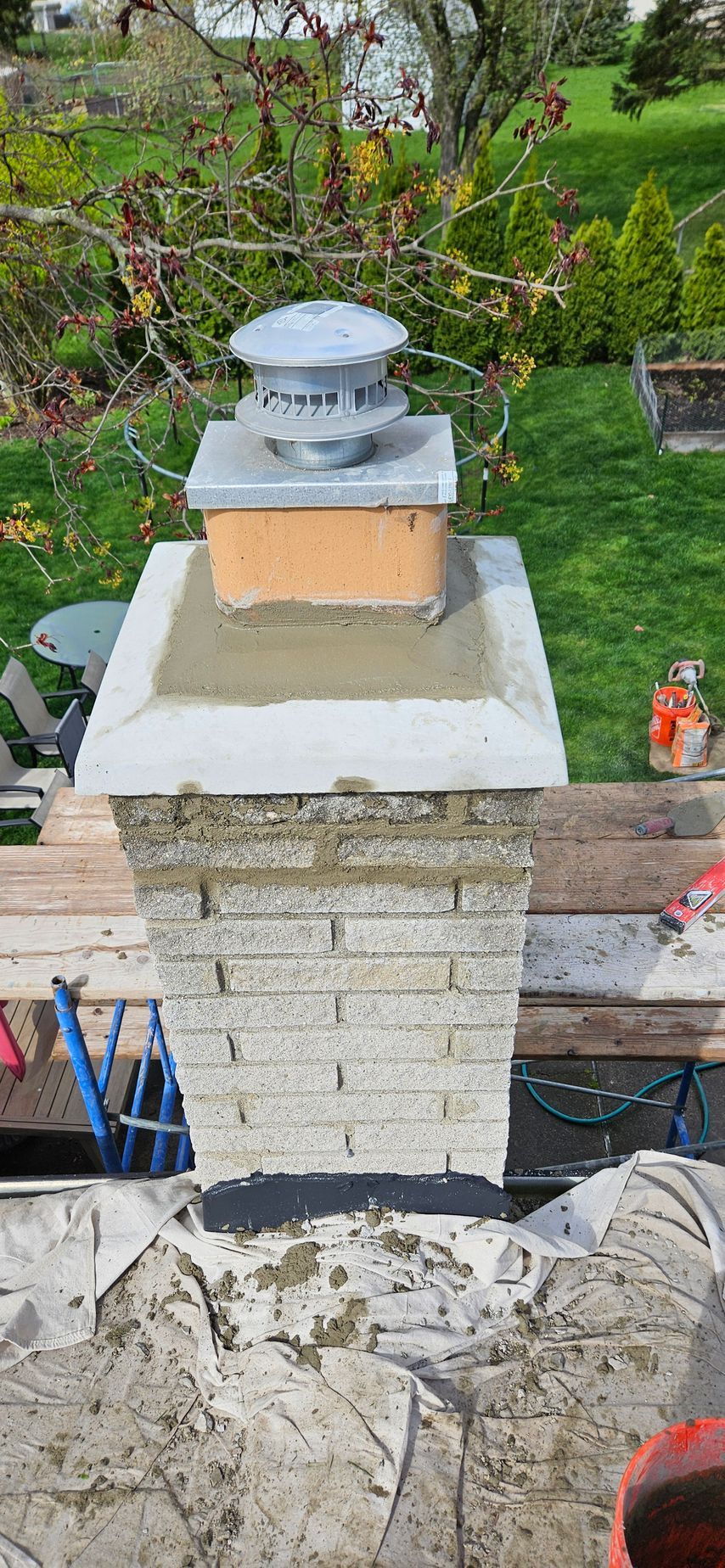 A brick chimney is being repaired in a backyard.