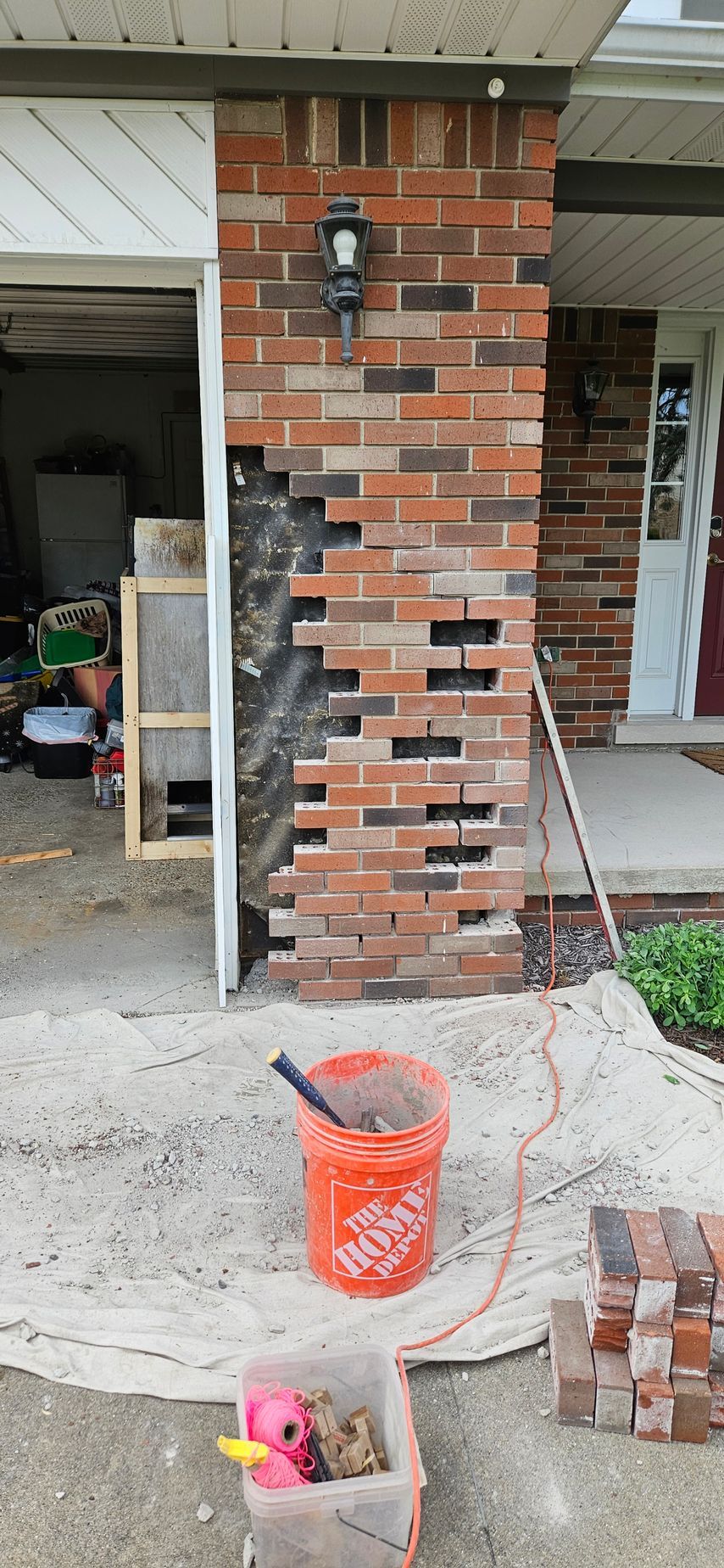 A bucket of home depot paint is sitting on the sidewalk in front of a brick wall.