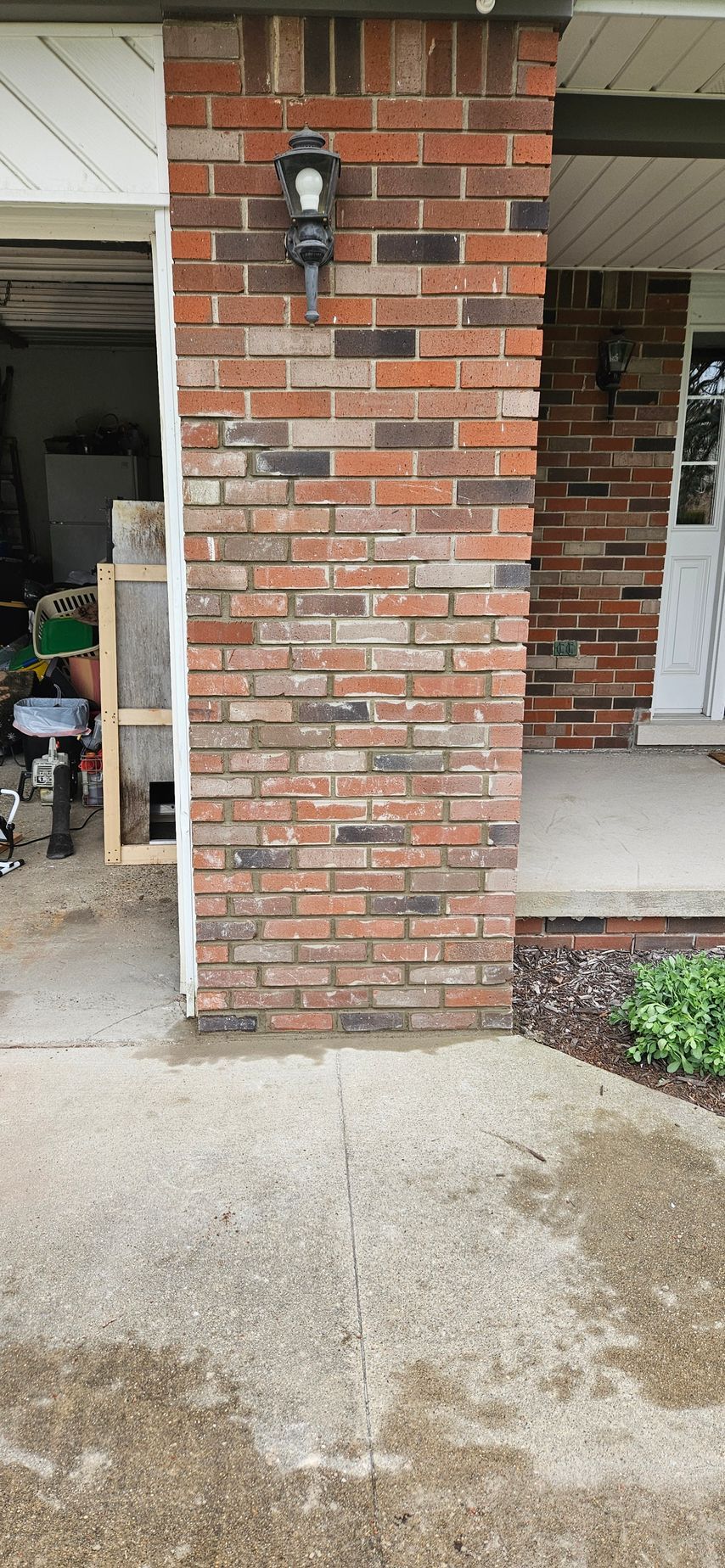 A brick wall with a lamp on it next to a porch.
