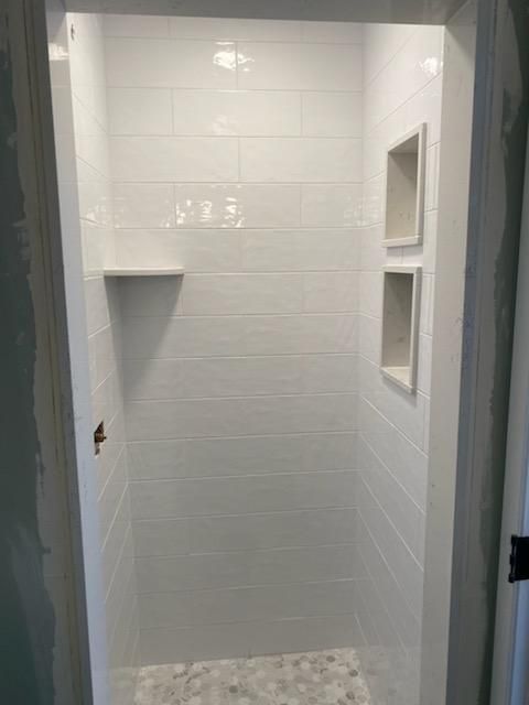 A bathroom with white tiles and a walk in shower.