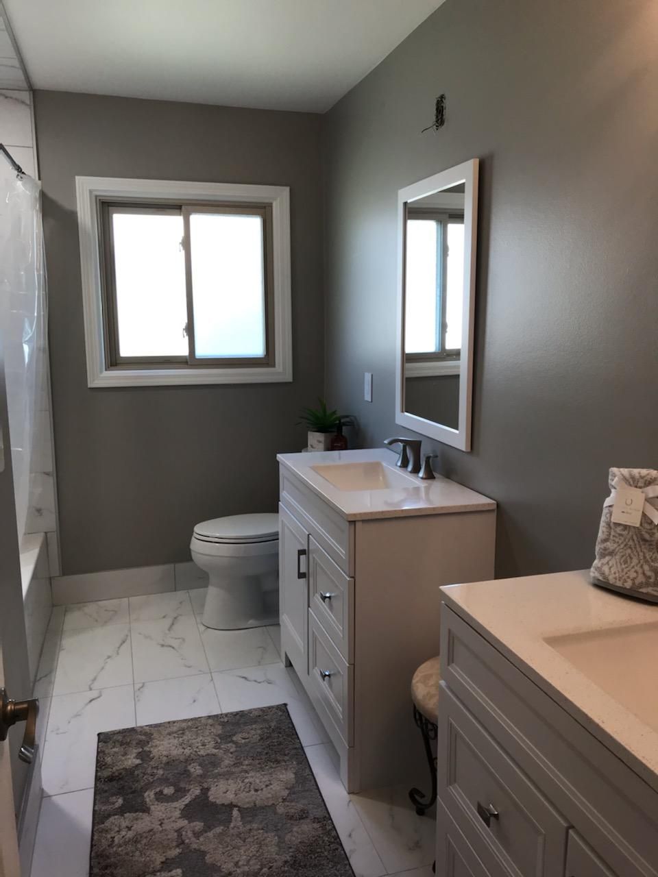 A bathroom with a toilet , sink , mirror and window.