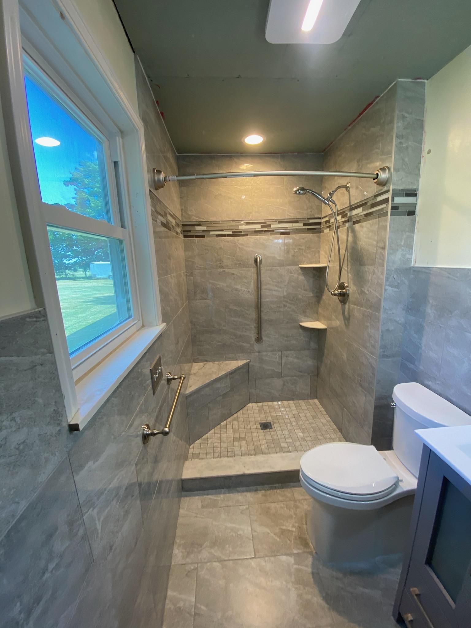A bathroom with a toilet , sink , shower and window.
