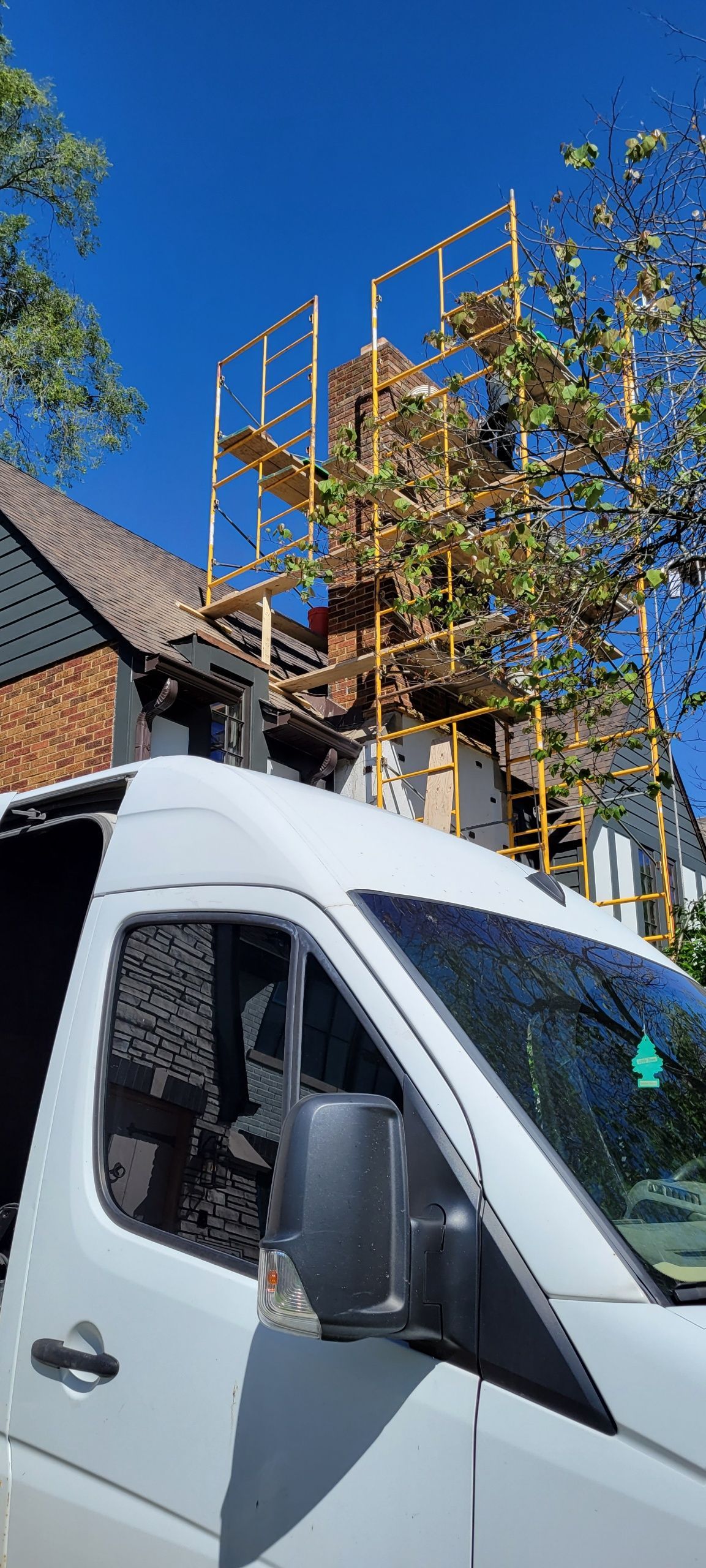 A white van is parked in front of a house with scaffolding on the roof.