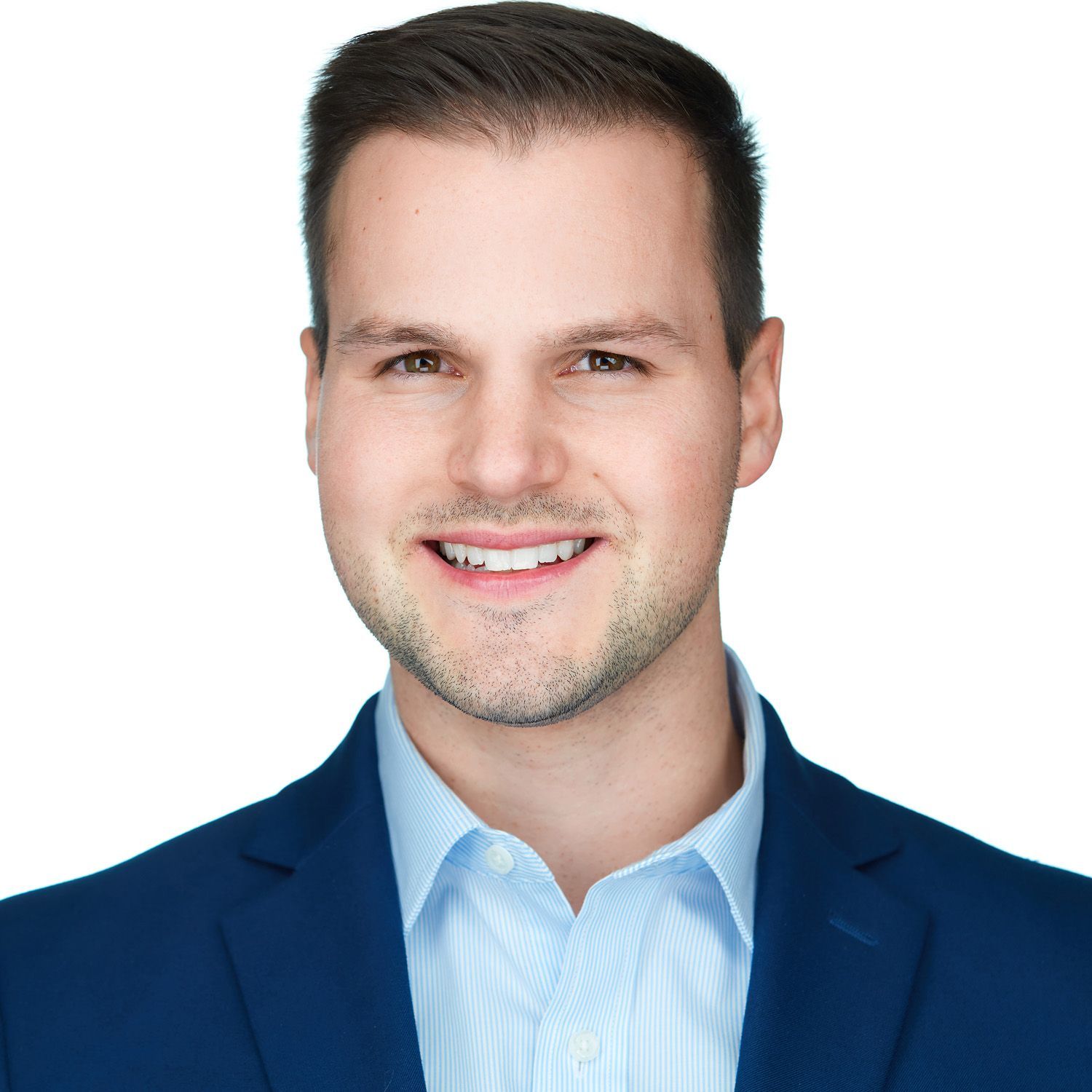 Man in a blue blazer and light blue shirt smiles, headshot against a white background.