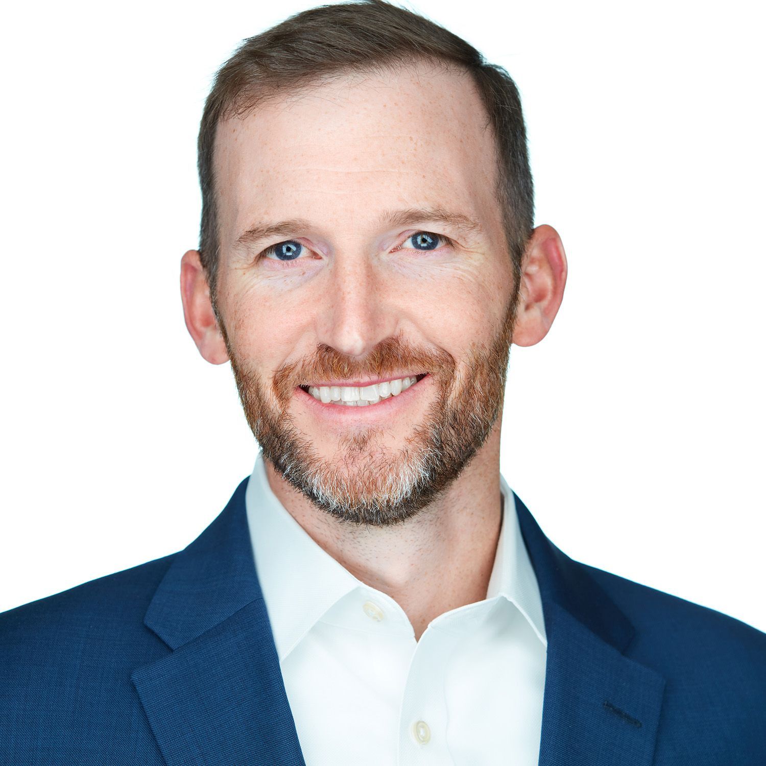 Man with a beard and blue blazer smiles, against a white background.