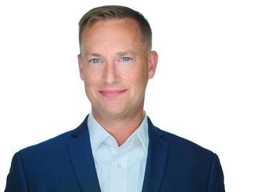 Man in a blue blazer and light blue shirt smiles, headshot against a white background.