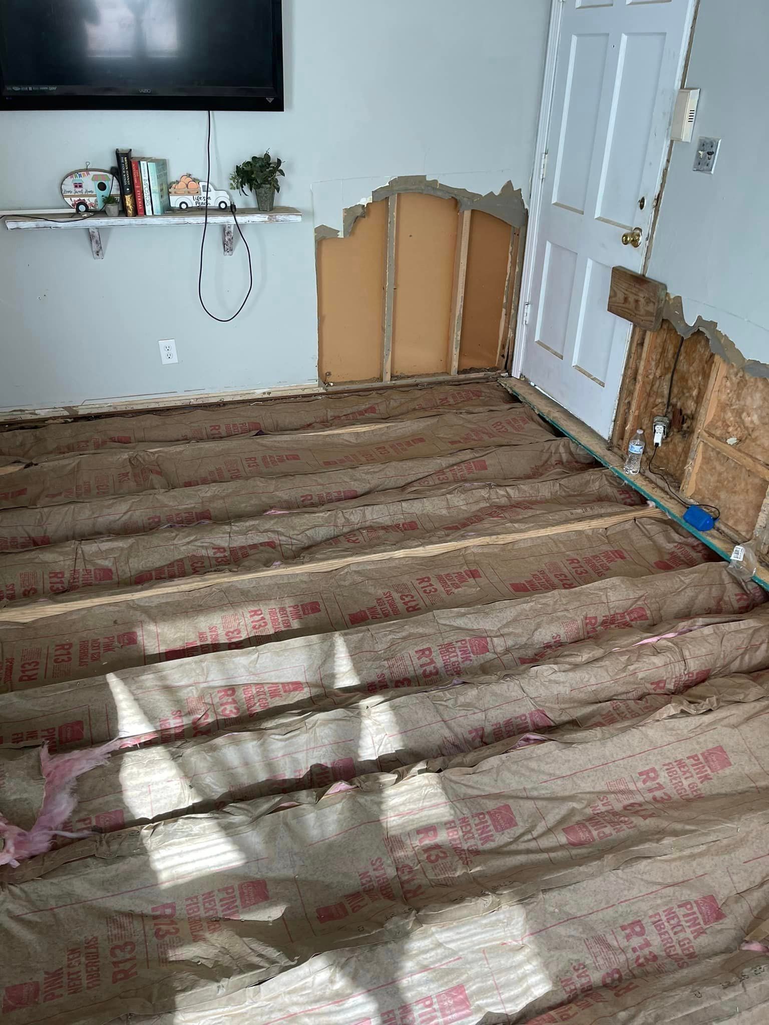 A living room with a broken wall and a wooden floor.