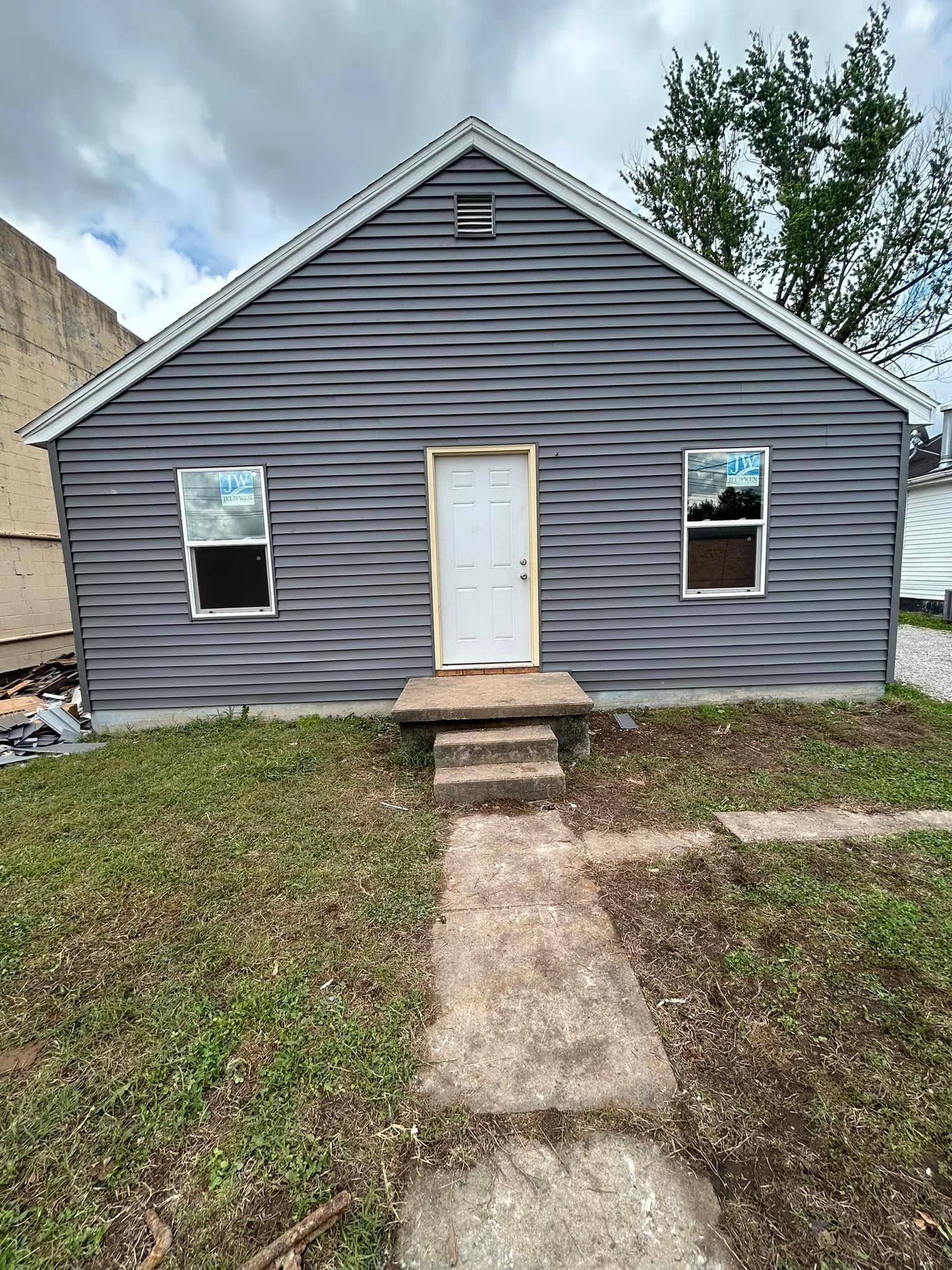 A small house with a concrete walkway leading to it is sitting on top of a lush green field.