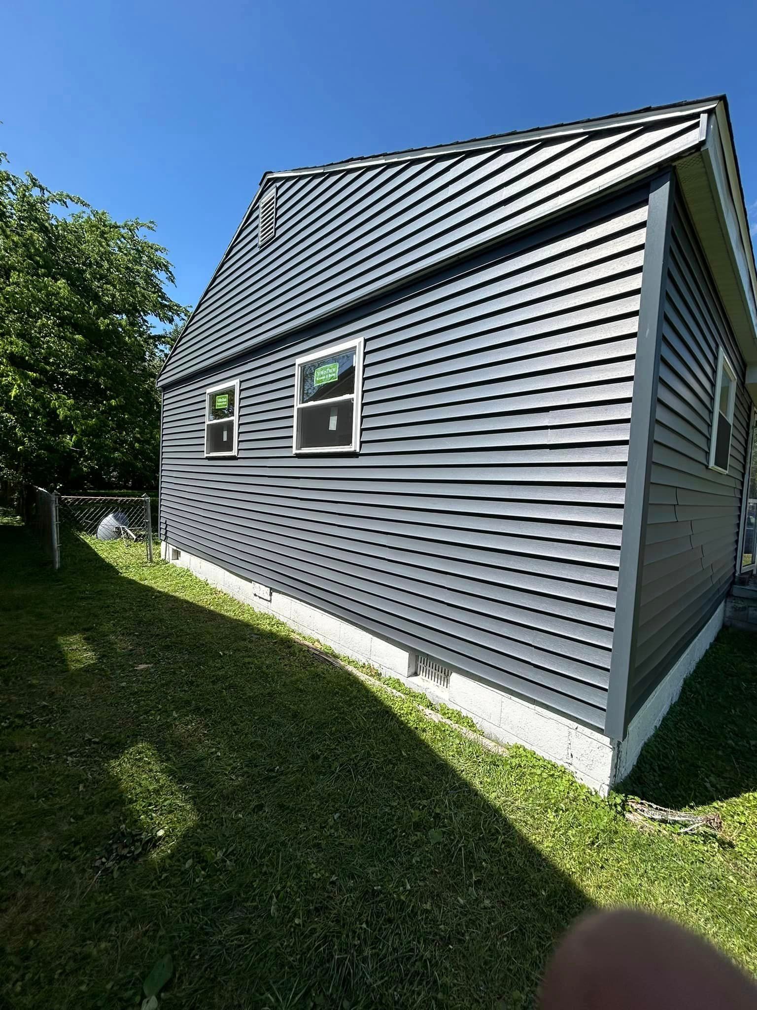 A large gray house with a lot of windows is sitting on top of a lush green lawn.
