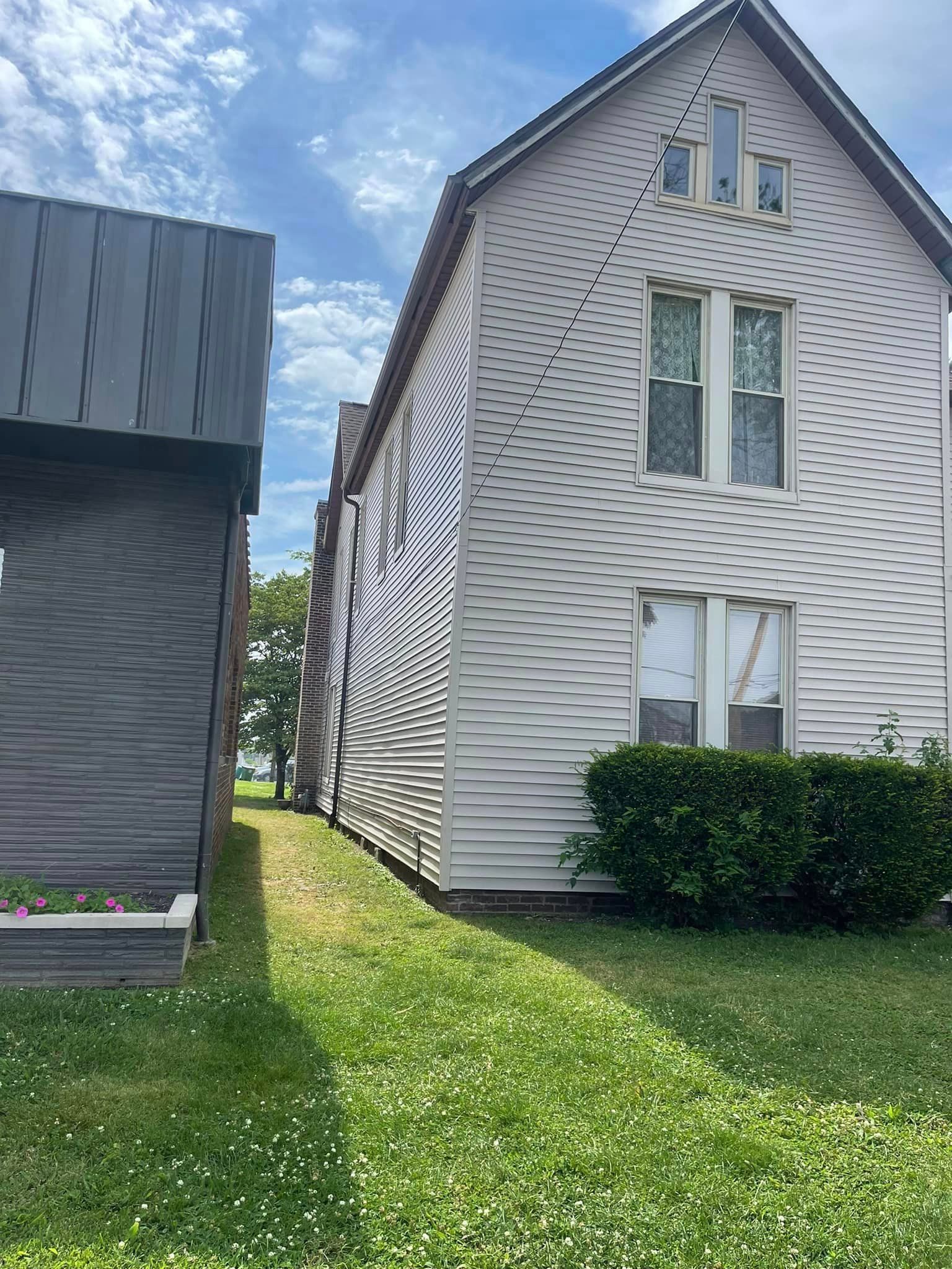 A white house with a gray roof is sitting next to a grassy field.